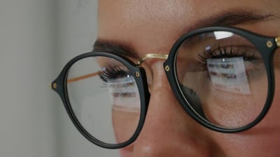 Close-up of a man's face wearing glasses that are reflecting his screen.