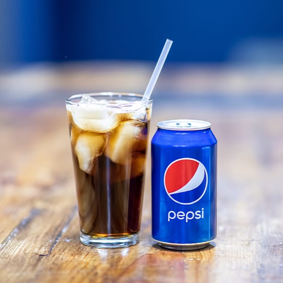 Pepsi can next to a glass full of Pepsi and ice