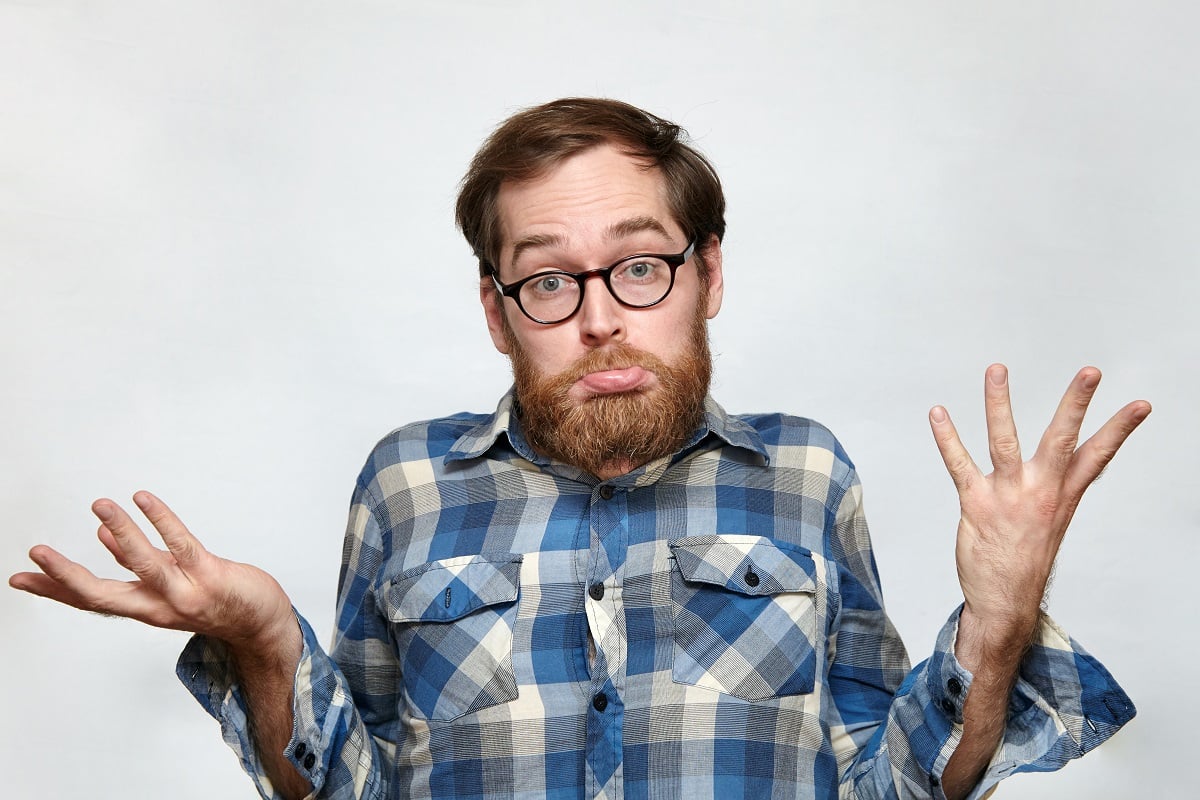 Man wearing glasses, in a blue checkered shirt shrugging his shoulders with his hand raised. He has a questionable/confused look on his face. 