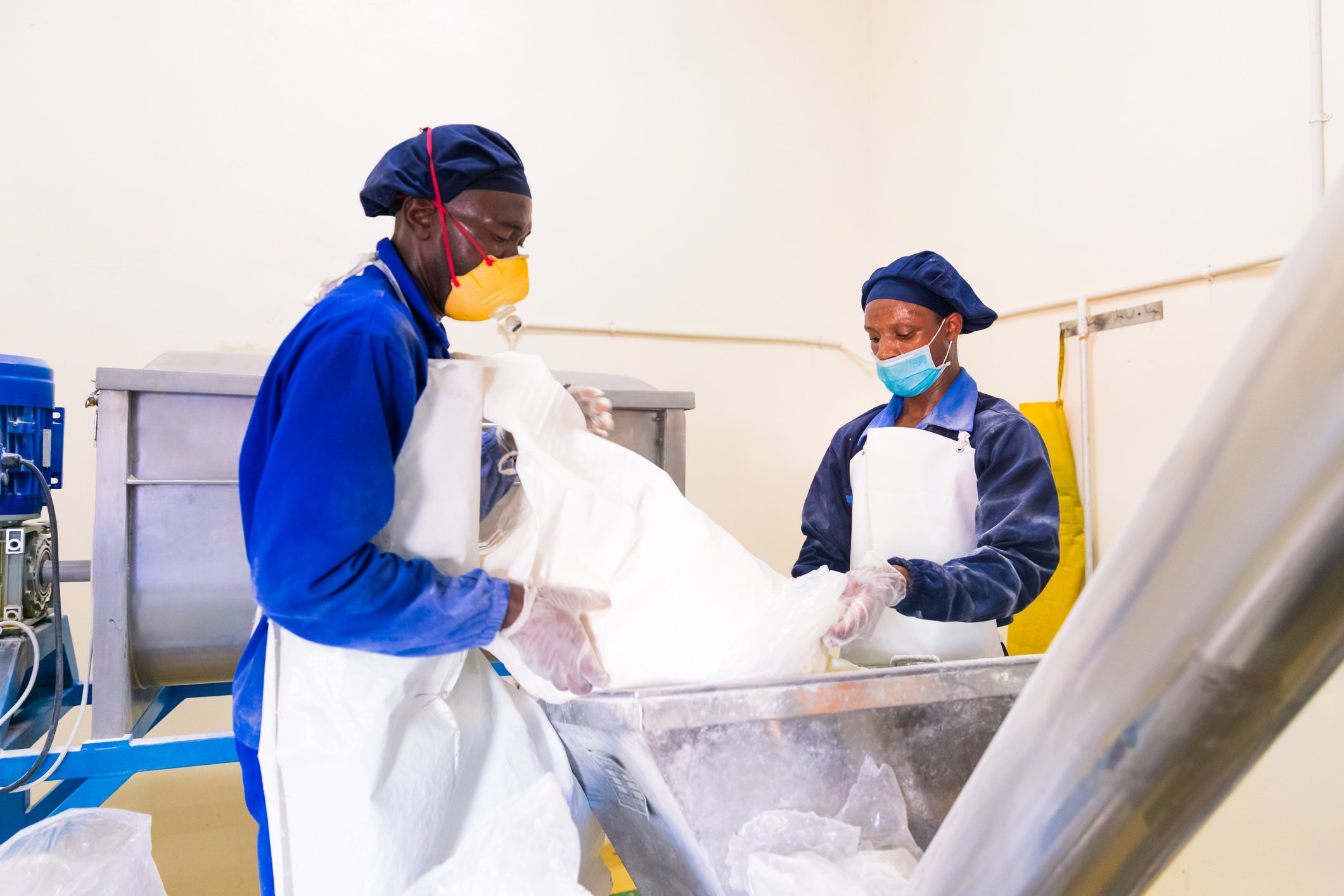 Two men in a factory pouring bulk powder into machine.