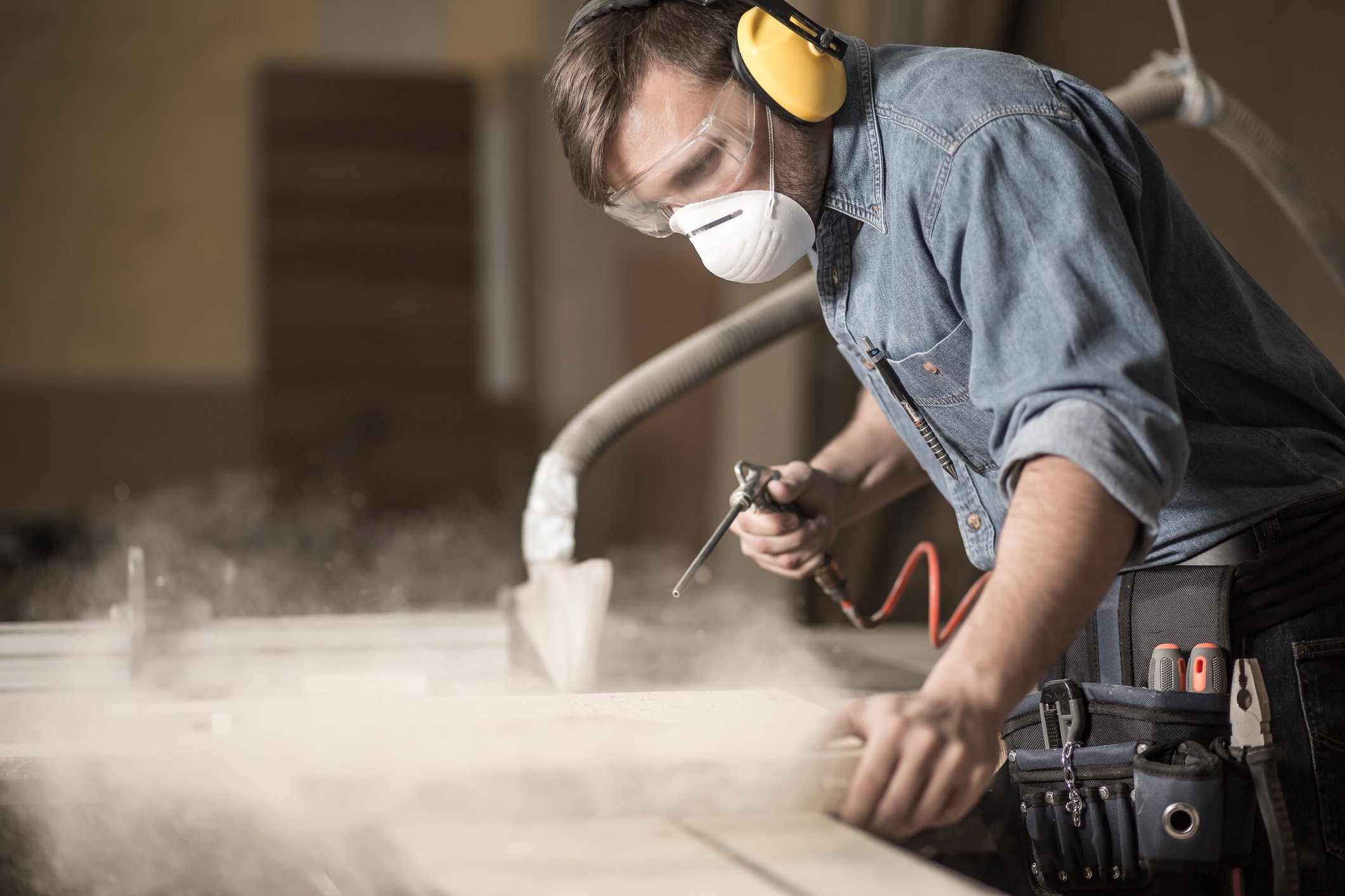 Masked man doing woodworking with fine dust particles in the air.