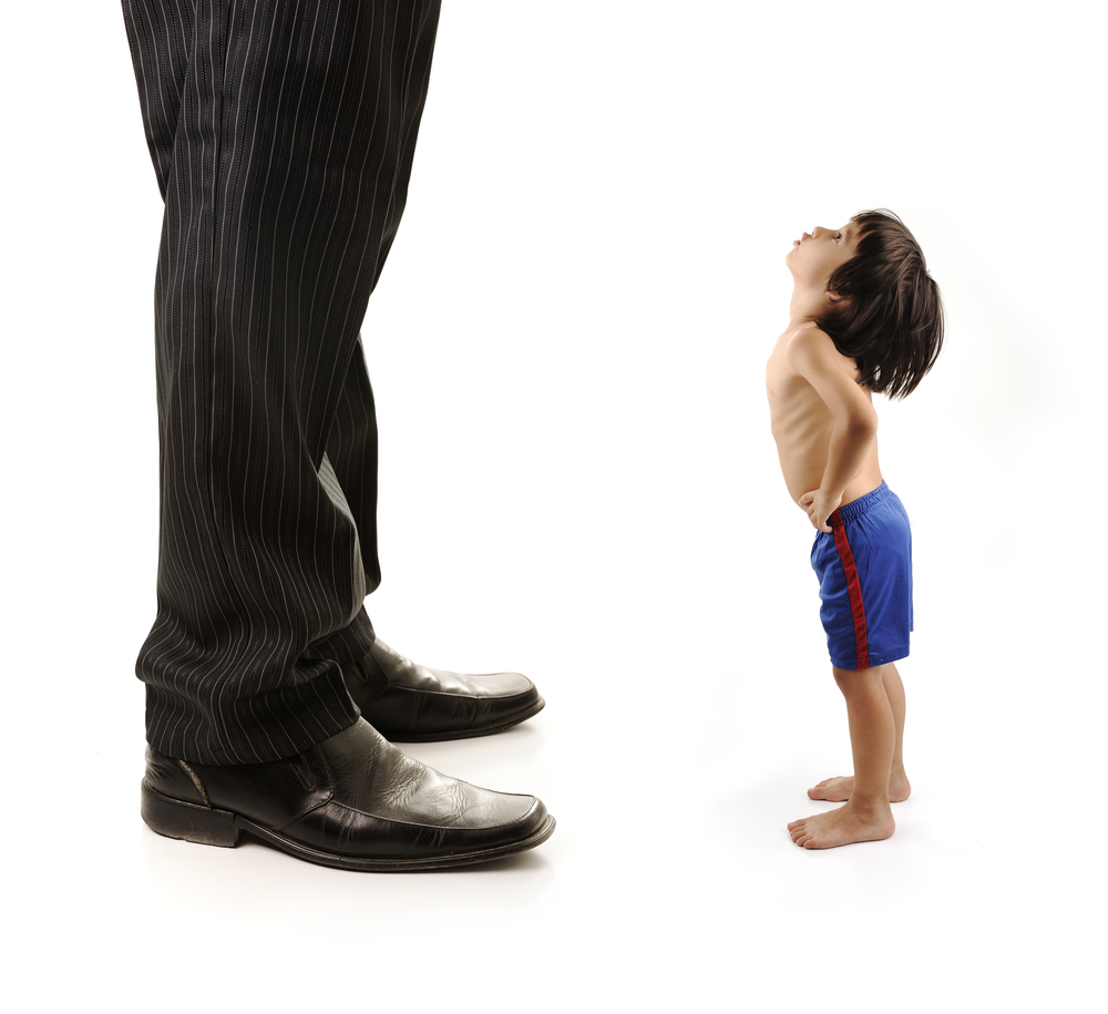 Little small child is looking at the giant legs of businessman adult