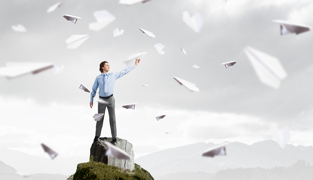 Young businessman on rock top with paper plane in hand