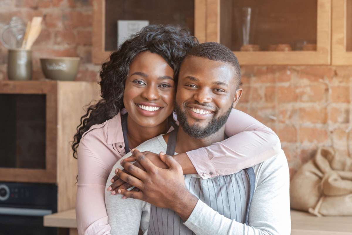 Beautiful african american woman hugging her husband from behind at kitchen