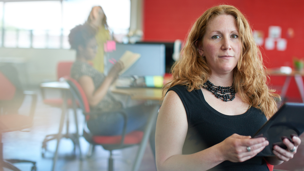 Confident female designer working on a digital tablet in red creative office space