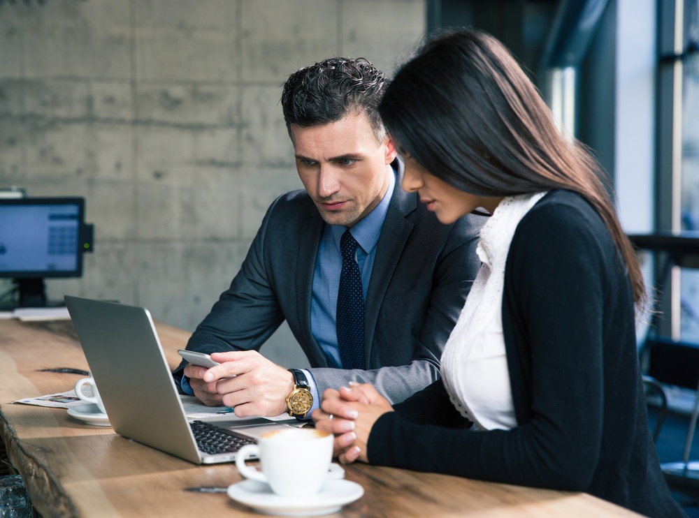 Handsome businessman and beautiful businesswoman using laptop together in cafe