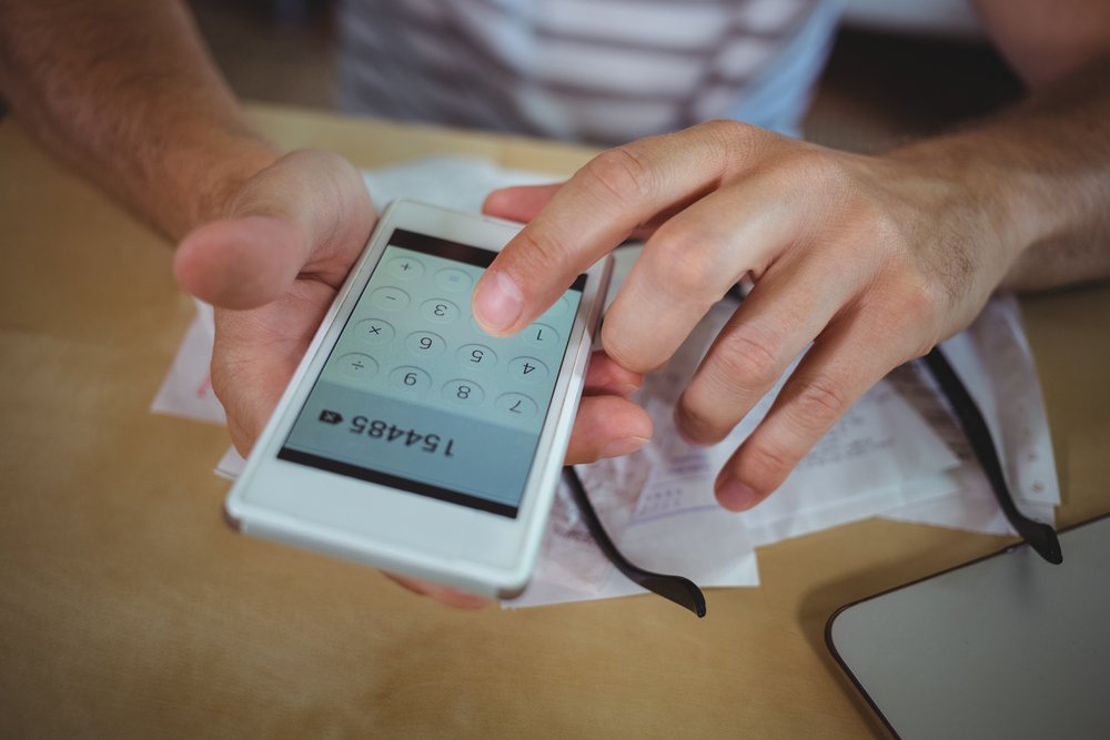 Mid section of man calculating bills on mobile phone-2