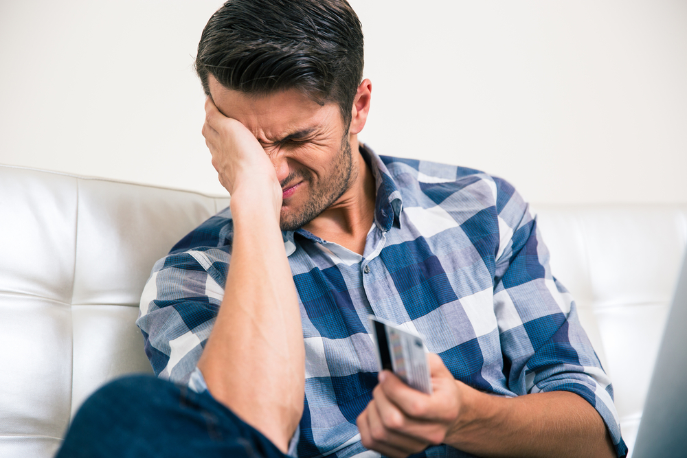 Portrait of a sad man holding bank card at home