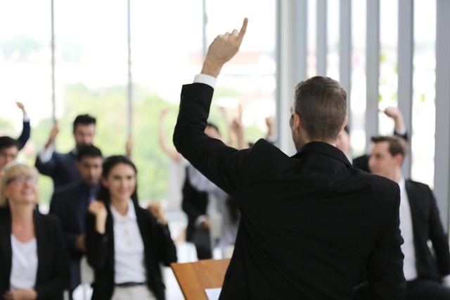 34895172_business-people-in-seminar-raising-hand-for-vote-at-meeting-activity-or-business-event-asking-question-at-speakers-seminar-or-workshop-min